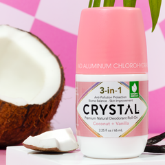 Pink Crystal deodorant bottle with Coconut Vanilla scent beside a halved coconut on a pink backdrop.