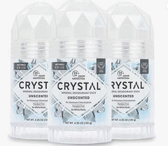 Three Crystal mineral deodorant sticks with unscented labels on a light geometric backdrop