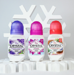 Three Crystal mineral-enriched deodorant roll-ons with purple, pink, and red caps on a white pedestal against a snowy backdrop