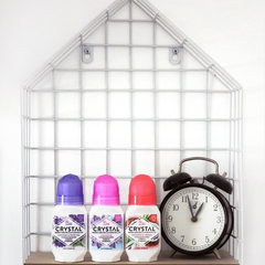 Crystal deodorant bottles with purple pink and red caps on a shelf beside a black alarm clock in a white wireframe display
