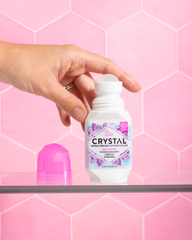 Hand pressing the cap on a Crystal mineral enriched deodorant bottle against a pink hex tile backdrop.