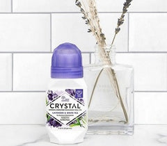 Crystal lavender deodorant bottle with purple cap on a white tiled counter beside a glass vase with dried stems.