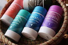Assorted Crystal deodorants in a woven basket with teal turquoise blue pink and purple bottles