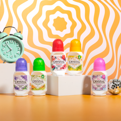 Assorted Crystal mineral deodorant bottles with colorful caps displayed on a bright orange patterned backdrop
