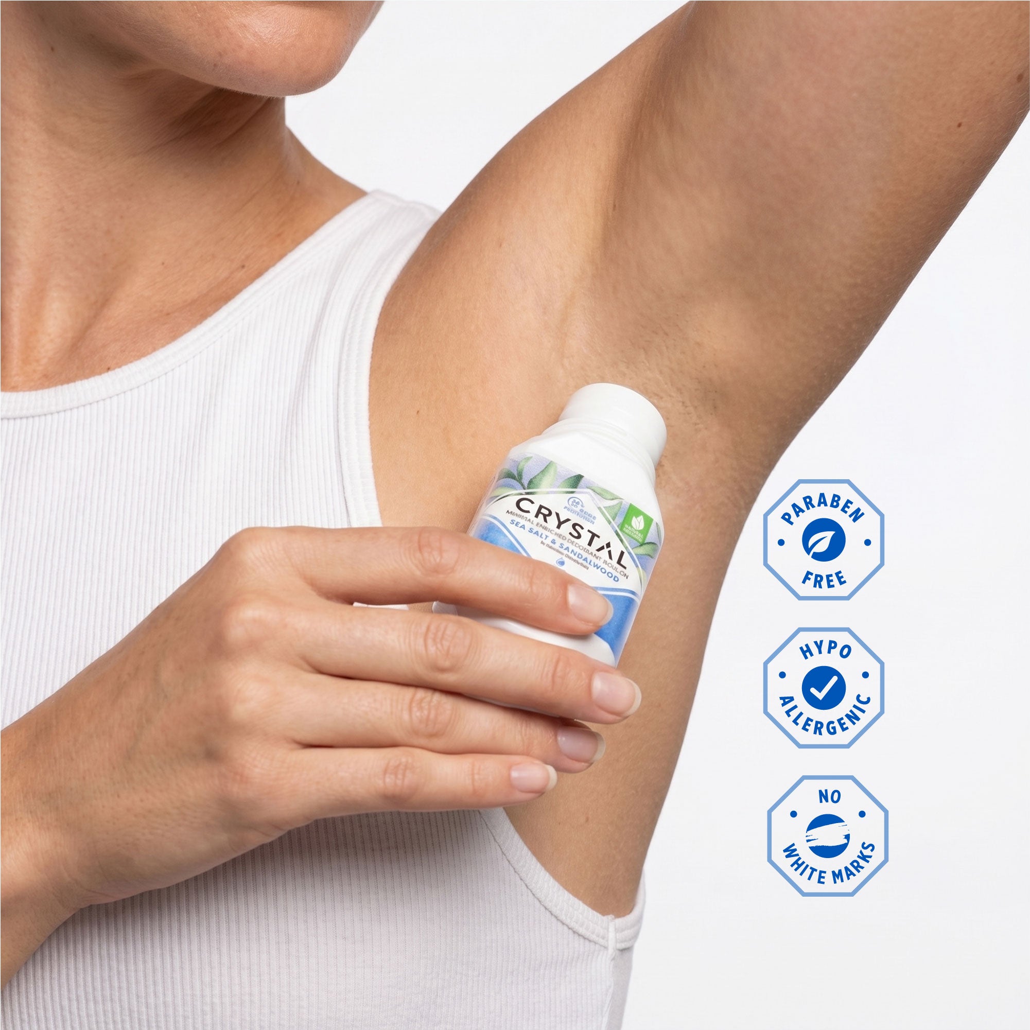 Person applying a bottle of Crystal deodorant to their under arm with product features displayed.