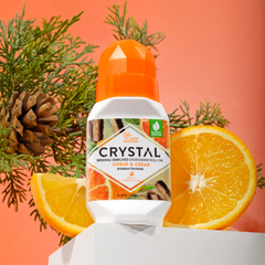 Crystal bottle of deodorant with oranges and greenery on an orange background