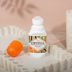 Crystal bottle of mineral-enriched deodorant roll-on on a decorative stone surface with an orange lid.