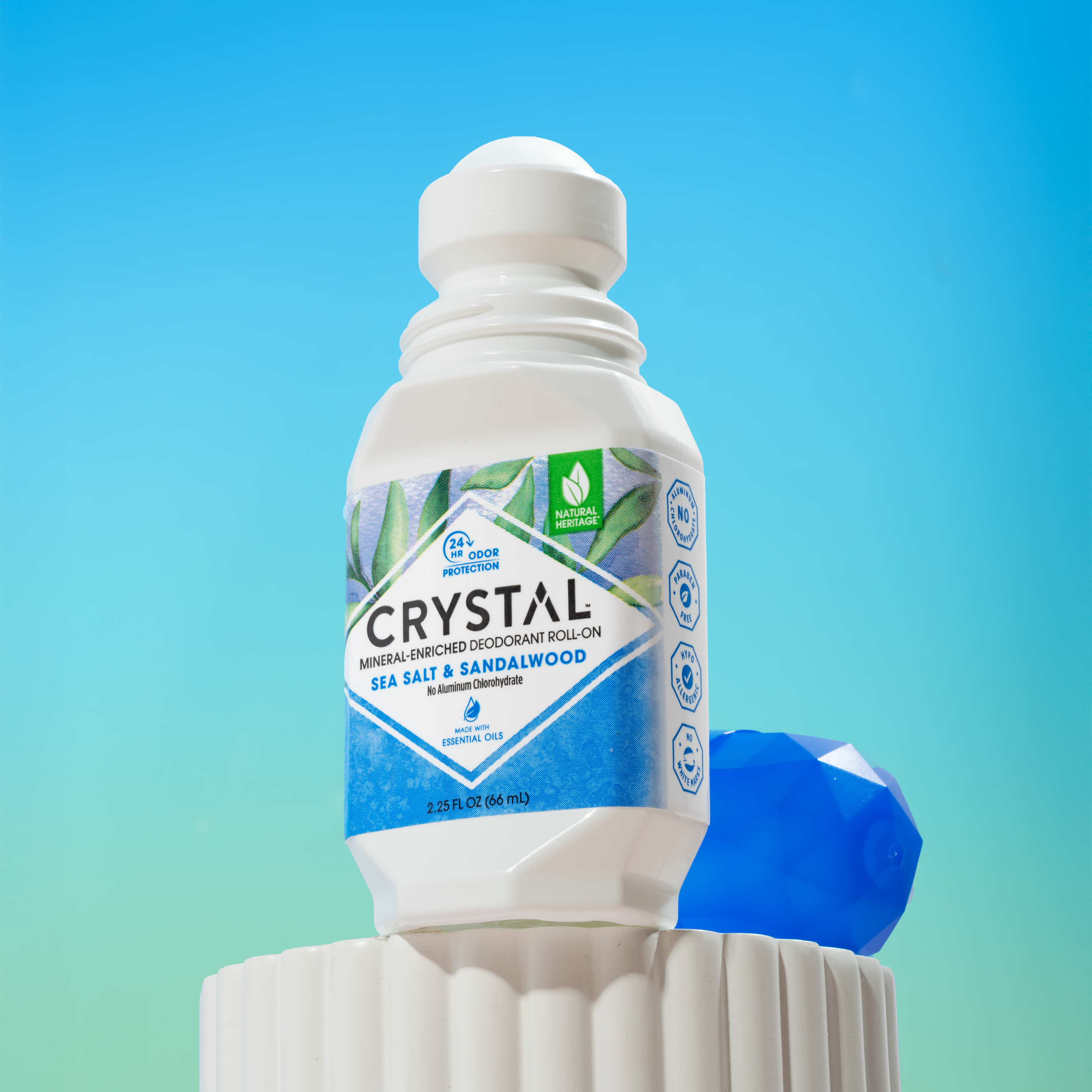 Bottle of Crystal Sea Salt & Sandalwood product on a decorative pedestal with a gradient blue and green background.